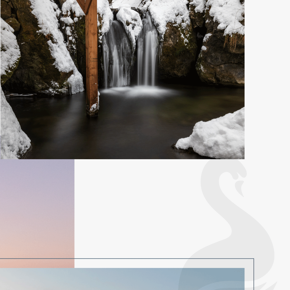 Landschaftsfoto von einem Wasserfall im Winter umrandet von Schneebedeckten Steinen